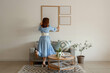 © Pixel-Shot - Young woman hanging big blank frame on light wall at home, back view