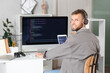 © Pixel-Shot - Young bearded programmer with headphones working at table in office