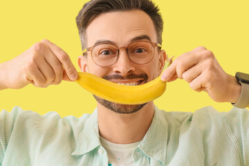 Canvas Print - Young man with banana on yellow background, closeup