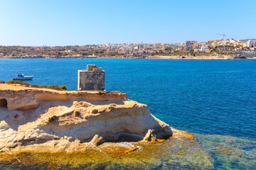 Wall Mural - St Thomas Bay and Marsaskala city view in Malta. Rocky cliff overlooks a body of water. The water is calm and blue, and there are a city in the distance