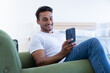 © Wavebreak Media - Smiling man relaxing on green sofa, using smartphone for entertainment at home