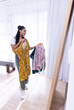 © Wavebreak Media - Choosing outfits, woman holding dresses and looking in mirror at home