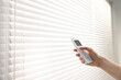 © New Africa - Woman using remote control to adjust window blinds indoors, closeup. Space for text