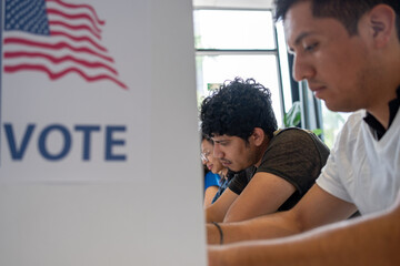 hispanic young man is seen intently casting his vote in a u.s. election. the voting booth is adorned