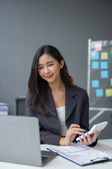 Wall Mural - Asian businesswoman works on laptop and calculates with financial calculator from graphs, statistics, charts. Planning. Business success results in modern office.