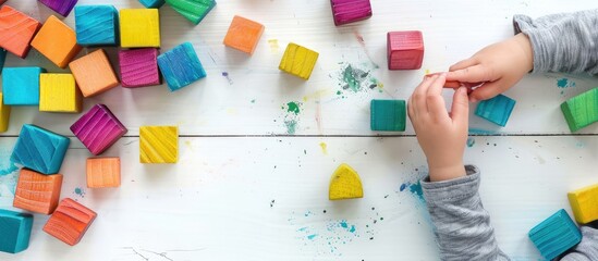 Poster - Child playing with vibrant wooden toy blocks on a white background wooden table, perfect copy space image.