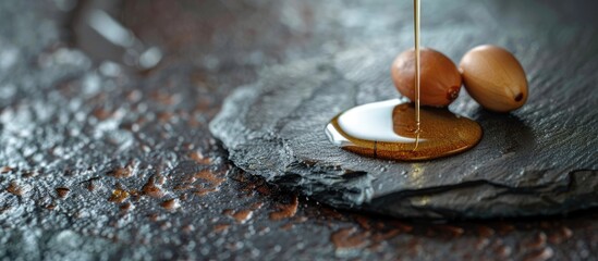 Leinwandbilder - Argan oil drizzling over two seeds on a stone table with copy space image.
