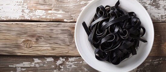Aufkleber - Black pasta on a white plate with a wooden background, top view, showcasing a free copy space image.
