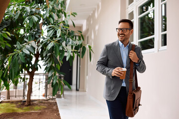 Happy businessman carrying takeaway coffee while coming to  office.