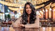 A young woman with long dark hair smiling and sitting at a table in a cafe