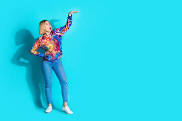 Sticker - Full size photo of impressed girl dressed print shirt jeans arm demonstrate big product empty space isolated on blue color background