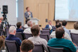 © Anton Gvozdikov - Business professionals attending a tech conference presentation with focus on the speaker and audience interaction.