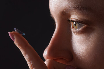 woman puts on contact lenses for vision close-up on a dark background, macro photo of contact lenses