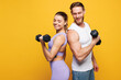 © ViDi Studio - Side view young strong fitness trainer instructor sporty two man woman wear blue clothes spend time in home gym hold in hand dumbbells isolated on plain yellow background. Workout sport fit concept.