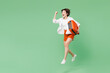 © ViDi Studio - Full body excited traveler woman wear casual clothes hold suitcase bag run fast hurry up jump high isolated on plain green background. Tourist travel abroad in free time rest. Air flight trip concept.