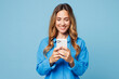 © ViDi Studio - Young smiling happy cheerful woman she wear shirt casual clothes hold in hand use mobile cell phone chat online isolated on plain pastel light blue cyan background studio portrait. Lifestyle concept.
