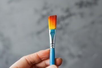 Poster - A small paintbrush with colorful bristles is held by a hand against a high-key, minimalistic background.