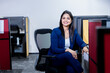 © GAJENDRRA BHATI  - young indian woman sitting on chair in office smiling looking at camera. corporate and workspace concept.