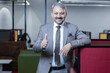 © GAJENDRRA BHATI  - happy indian senior businessman thumbs up standing in corporate office and looking at camera. business and workplace concept.