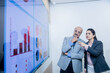 © GAJENDRRA BHATI  - young indian professional woman with businessman discussing trading and stocks in office. Stock brokers looking at indexes graphs on big computer screen