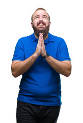 Poster - Young caucasian hipster man wearing blue shirt over isolated background begging and praying with hands together with hope expression on face very emotional and worried. Asking for forgiveness.