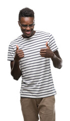 Wall Mural - Young african american man wearing glasses and navy t-shirt success sign doing positive gesture with hand, thumbs up smiling and happy. Looking at the camera with cheerful expression, winner gesture.