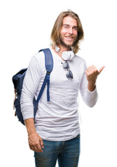 Poster - Young handsome tourist man with long hair wearing backpack over isolated background smiling with happy face looking and pointing to the side with thumb up.