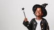© Kanlayarawit - A cute and happy African American black boy wearing a witch hat and dressing like a wizard in a Halloween costume holding a wand on a plain white background with copy space for text.