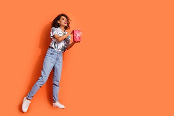 Wall Mural - Photo of young beautiful happy girl wavy hairstyle holding birthday surprise looking empty space at store isolated on orange color background