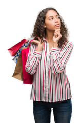 Canvas Print - Young hispanic woman holding shopping bags serious face thinking about question, very confused idea