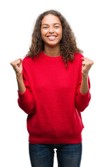 Sticker - Young hispanic woman wearing red sweater celebrating surprised and amazed for success with arms raised and open eyes. Winner concept.