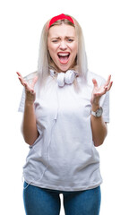 Canvas Print - Young blonde woman wearing headphones listening to music over isolated background crazy and mad shouting and yelling with aggressive expression and arms raised. Frustration concept.