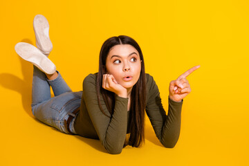 Sticker - Full body photo of attractive teen woman lying floor point look empty space shock dressed khaki clothes isolated on yellow color background