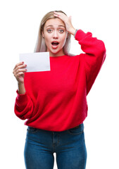 Canvas Print - Young blonde woman holding blank paper card over isolated background stressed with hand on head, shocked with shame and surprise face, angry and frustrated. Fear and upset for mistake.