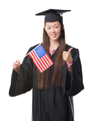 Canvas Print - Young Chinese woman wearing graduate uniform holding United states of america flag happy with big smile doing ok sign, thumb up with fingers, excellent sign