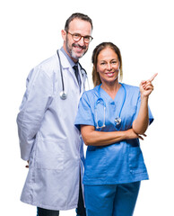 Canvas Print - Middle age hispanic doctors partners couple wearing medical uniform over isolated background with a big smile on face, pointing with hand and finger to the side looking at the camera.