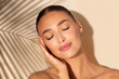 © Home-stock - Young European woman with closed eyes and healthy clear skin posing on beige background with palm leaf shadow. Cosmetic, skincare, spa concept.