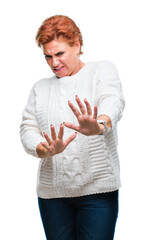 Wall Mural - Atrractive senior caucasian redhead woman wearing winter sweater over isolated background disgusted expression, displeased and fearful doing disgust face because aversion reaction. With hands raised.