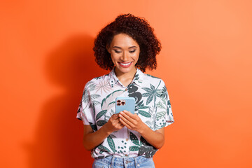 Wall Mural - Photo of young brown haired curly lady in summertime season style shirt using smartphone using twitter isolated on orange color background