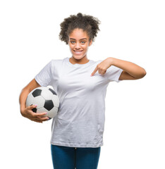 Sticker - Young beautiful afro american holding soccer football ball over isolated background with surprise face pointing finger to himself