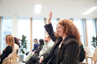 © Johnér - Smiling young businesswoman raising hand during meeting in office