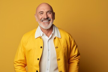 Wall Mural - Portrait of a smiling man in his 50s sporting a stylish varsity jacket isolated on pastel yellow background