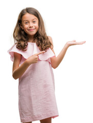 Wall Mural - Brunette hispanic girl wearing pink dress amazed and smiling to the camera while presenting with hand and pointing with finger.