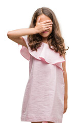 Poster - Brunette hispanic girl wearing pink dress smiling and laughing with hand on face covering eyes for surprise. Blind concept.