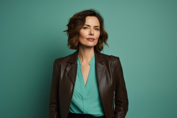Wall Mural - Portrait of a glad woman in her 40s sporting a stylish leather blazer in front of pastel teal background