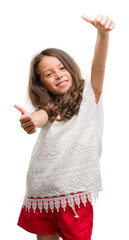 Sticker - Brunette hispanic girl approving doing positive gesture with hand, thumbs up smiling and happy for success. Looking at the camera, winner gesture.