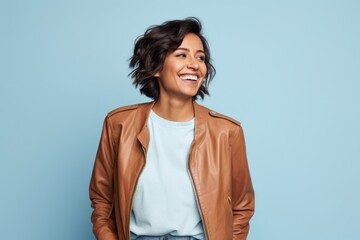 Wall Mural - Portrait of a jovial indian woman in her 30s wearing a trendy bomber jacket isolated on soft blue background