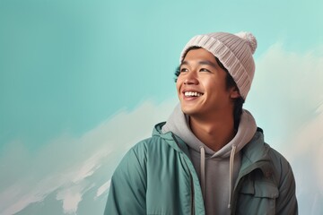 Wall Mural - Portrait of a joyful asian man in his 20s dressed in a warm ski hat over soft teal background