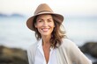 © Markus Schröder - Portrait of a smiling woman in her 40s donning a classic fedora over serene seaside background