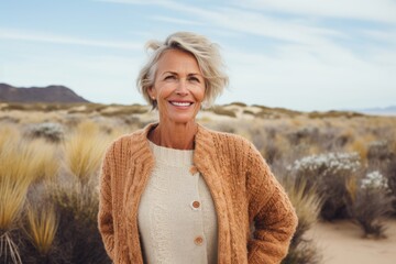 Wall Mural - Portrait of a cheerful woman in her 50s wearing a chic cardigan over serene dune landscape background